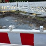 Eine mit Schotter gefüllte Baugrube, umgeben von weiß-roten Absperrgittern