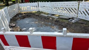 Eine mit Schotter gefüllte Baugrube, umgeben von weiß-roten Absperrgittern